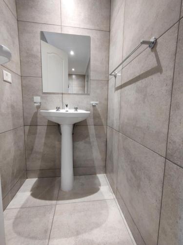 uma casa de banho com um lavatório e um chuveiro com um espelho. em Amigo del Mundo Hostería y Apart Hotel em El Calafate