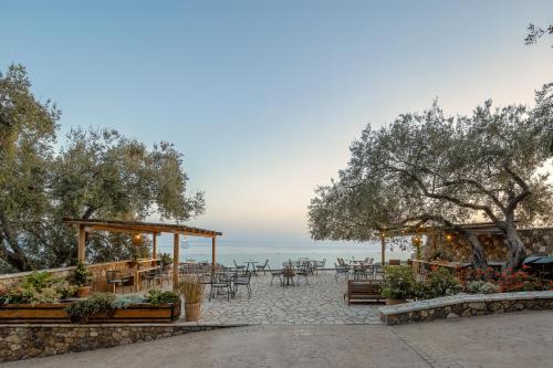eine Terrasse mit Tischen, Bäumen und dem Meer in der Unterkunft Apolis Villas & Suites Resort in Parga