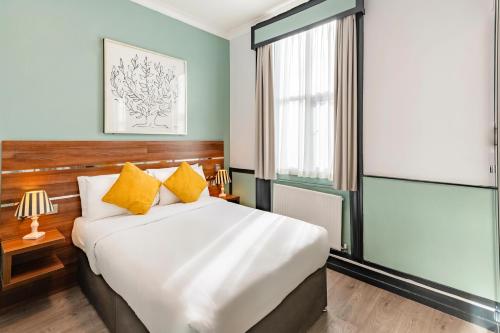 een slaapkamer met een groot wit bed met gele kussens bij Huttons Hotel, Victoria London in Londen