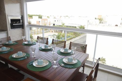 a wooden table with plates and wine glasses on a balcony at Apartamento na Praia do Francês in Marechal Deodoro