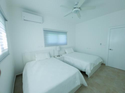 a white bedroom with two beds and a window at 2JA Management Group - Condos White Hill in Sosúa