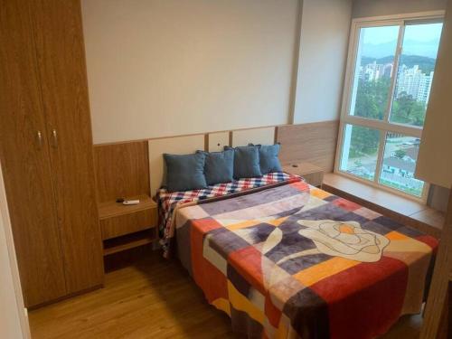 a bedroom with a bed with a colorful blanket and a window at Apto Completo Centro Joinville in Joinville
