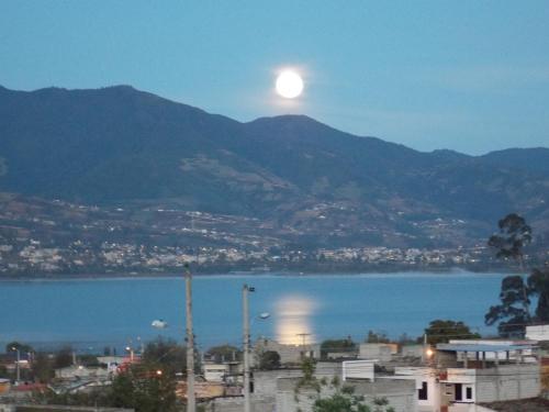 a full moon rising over a city and a body of water at Green House Araque Inn in Otavalo