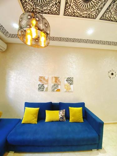 a blue couch with yellow pillows and a chandelier at Appartement calme in Fez