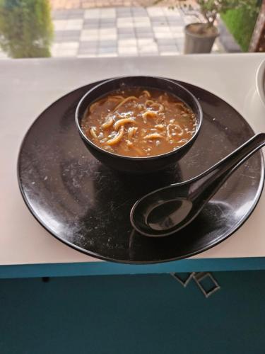 a bowl of soup on a black plate with a spoon at Hotel Sai Dakshina Inn & The Fern Restaurant in Shirdi