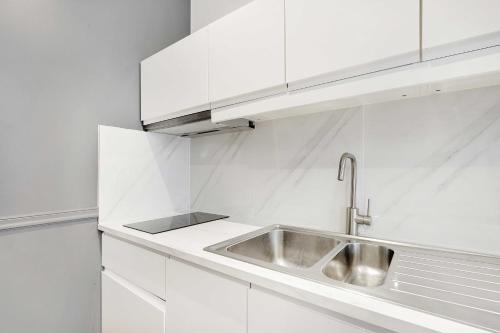 - une cuisine blanche avec un évier et des placards blancs dans l'établissement Résidence Boulanger - République, à Paris