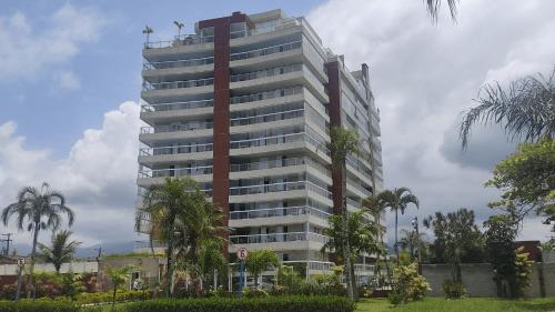 a tall building with palm trees in front of it at Doce Lar de Bertioga Frente ao Mar (Indaiá) in Bertioga