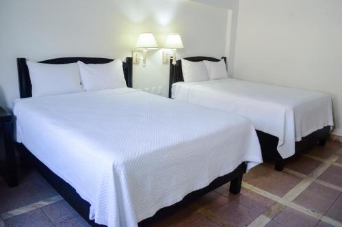 two beds in a hotel room with white sheets at Hotel Armida Guaymas in Guaymas