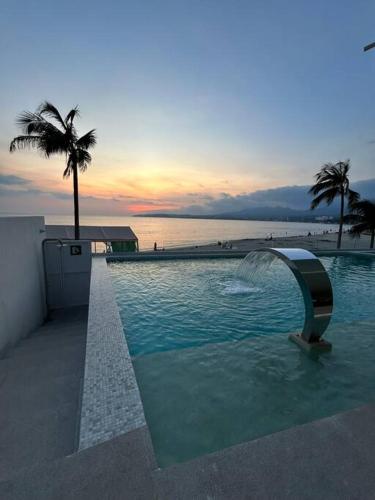 a swimming pool with a fountain and a palm tree at Departamento Cielo Bucerias, Beach Front Nayarit in Bucerías
