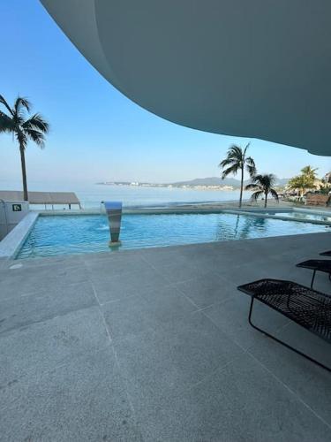 a swimming pool with palm trees and the ocean at Departamento Cielo Bucerias, Beach Front Nayarit in Bucerías