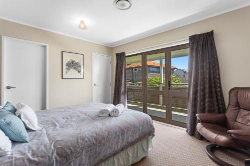 a bedroom with a bed and a chair and a window at The Sun Capsule - Ohope Beach Holiday Home in Ohope Beach