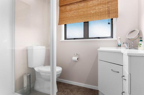 a white bathroom with a toilet and a window at The Sun Capsule - Ohope Beach Holiday Home in Ohope Beach