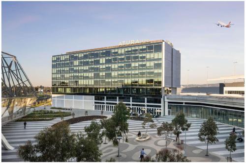 un gran edificio de cristal con un avión volando sobre él en Atura Adelaide Airport en Adelaida