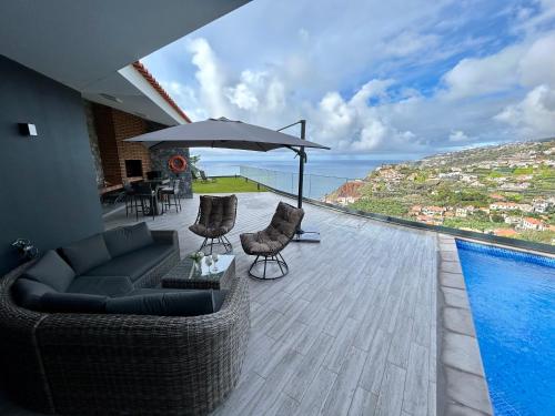 un patio con sofá, sombrilla y piscina en Villa Sol e Mar, en Ribeira Brava