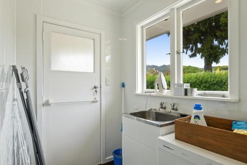 uma cozinha branca com um lavatório e uma janela em Kohekohe Garden Cottage - Waikanae Holiday Home em Waikanae