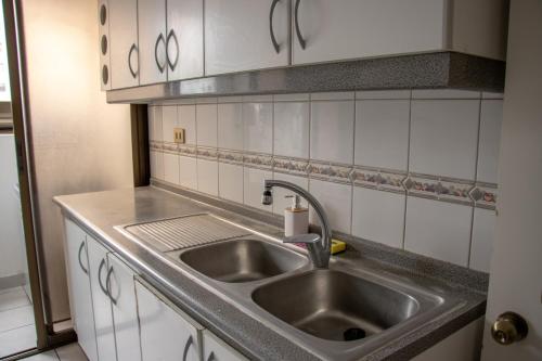 una cocina con fregadero de acero inoxidable y armarios blancos en Departamento royal marine, en Iquique