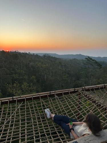 a woman laying on top of a viewing platform with the sunset at Wanagiri sunset glamping in Gitgit