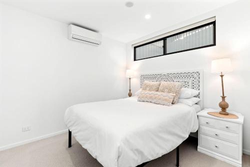 een witte slaapkamer met een wit bed en een raam bij Ohana Apartment 312 in Batemans Bay