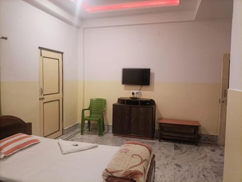 a bedroom with a bed and a tv and two green chairs at Hotel Sonali in Lataguri