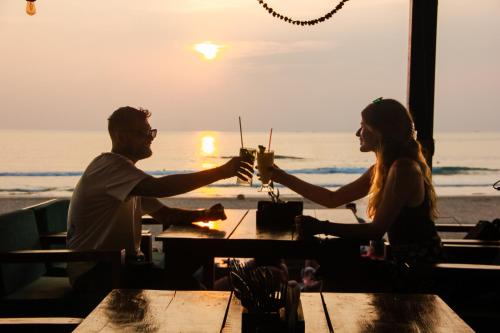 una pareja sentada en una mesa en la playa con bebidas en New Common Home, en Agonda