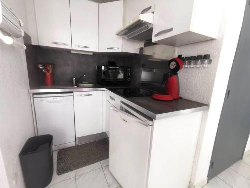 - une petite cuisine avec des placards blancs et un jouet rouge sur le comptoir dans l'établissement 039 Marina Bay 403, au Cap d'Agde