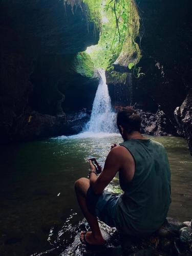 a man sitting in the water in front of a waterfall at EDRIAN BUNGALOWS in Tetebatu