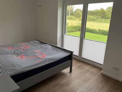 a bedroom with a bed and a large window at Haacksen - modernes Ferienhaus mit 4 Schlafzimmern, Garten und Grill in Klappholz