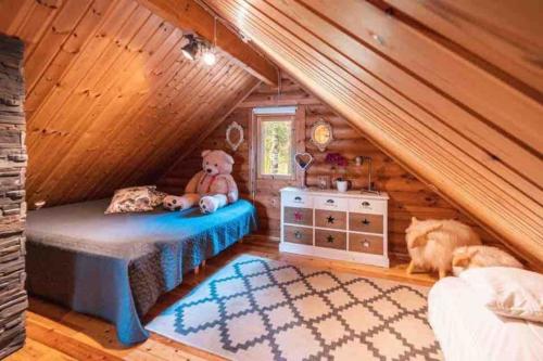 a teddy bear sitting on a bed in a cabin at Minivilla Peikonpesä ulkoporeallas & pihasauna in Loppi