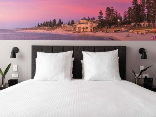 a bedroom with a white bed and a beach with a house at Novotel Perth Murray Street in Perth
