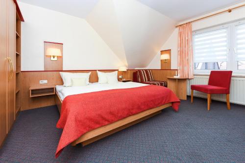 a hotel room with a bed and a red chair at Pension Nordkap in Bensersiel