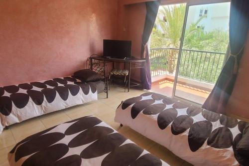 a room with two beds and a television and a balcony at Agadir Marina vue piscine in Agadir