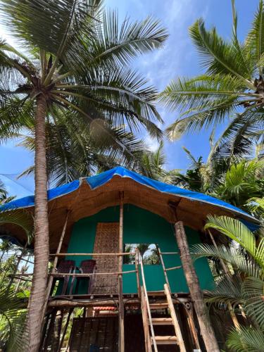 uma casa na árvore com um telhado azul e palmeiras em Hobknob, Goa - hostel with a pool em Nogorcem