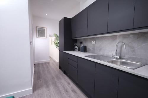 a kitchen with black cabinets and a sink at PrimeLocation! Spacious 4BR Apt Market St Watford! in Watford