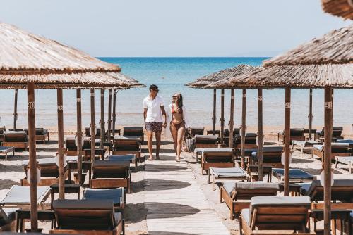two people walking on a beach with chairs and umbrellas at Almira Hotel in Arkoudi
