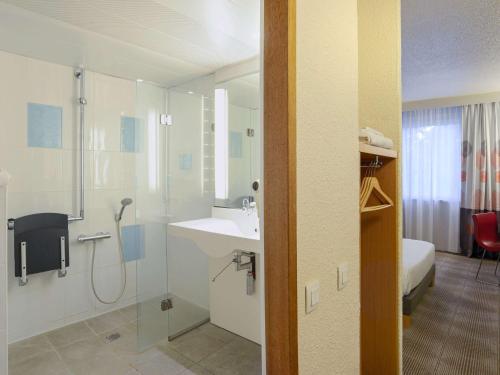 a bathroom with a shower and a sink and a bed at Novotel Toulouse Purpan Aéroport in Toulouse