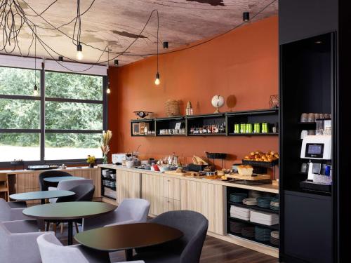 un restaurant avec des murs orange, des tables et des chaises dans l'établissement ibis Styles Lille Aéroport, à Lesquin