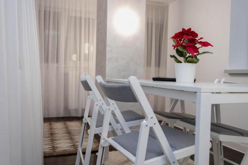 a white table with two chairs and a vase with a red flower at Exclusive Apartment in Giurgiu