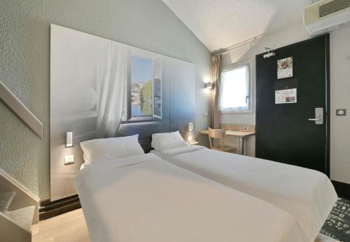 two white beds in a room with a window at B&B HOTEL Le Mans Sud in Arnage