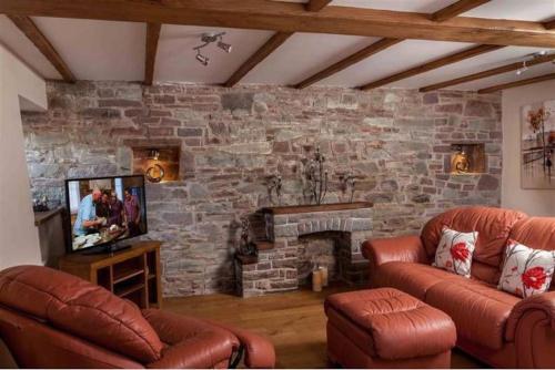 a living room with two leather couches and a stone wall at Trefaen Cottage in Brecon