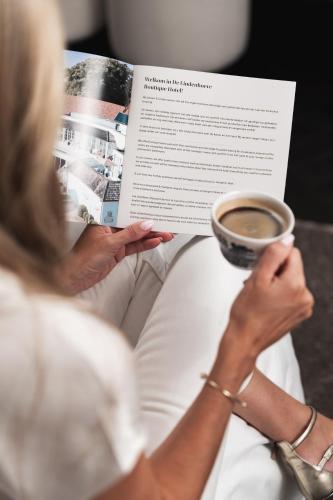 a woman reading a book with a cup of coffee at De Lindenhoeve Boutique Hotel in Sluis