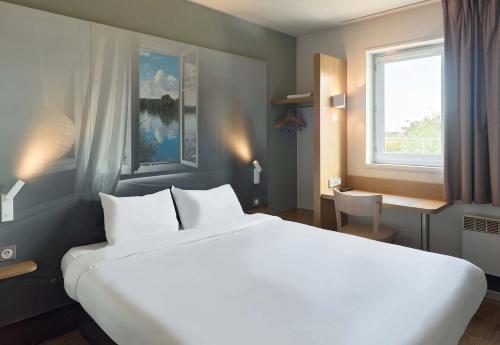 Un dormitorio con una gran cama blanca y una ventana en B&B HOTEL Evry Lisses 1 en Lisses