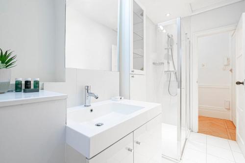 a white bathroom with a sink and a shower at Beautiful Belgravia Apartment by UnderTheDoormat in London