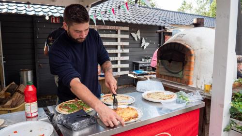 a man preparing pizzas in front of a pizza oven at Camping Emmen in Schoonebeek