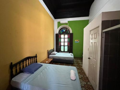 2 camas en una habitación con paredes verdes y ventana en Hostal Plaza Antigua, en Santa Ana