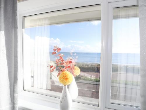 a white vase with flowers sitting on a window sill at 21 Min Y Mor in Pwllheli