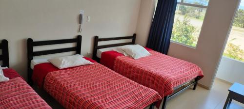 a room with two beds with red sheets and a window at Hotel Alta Vista Campestre in Tibasosa