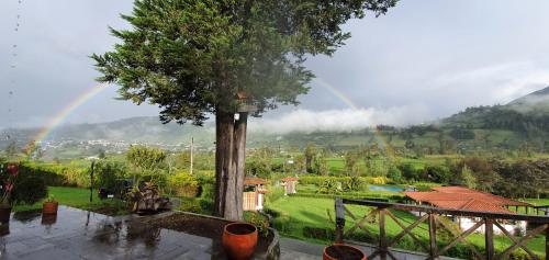 un arcobaleno sopra un giardino con una casa con un albero di Eco Avocado Lodge a San José de Minas