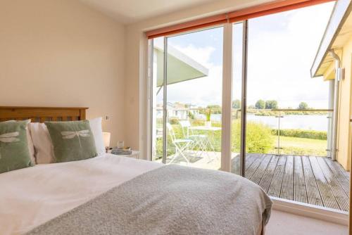 a bedroom with a bed and a large glass window at Tawny House CW6 Lakeside Spa Property in Somerford Keynes