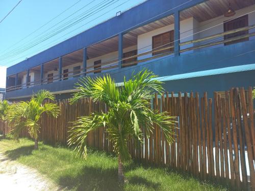 a blue building with palm trees in front of a fence at Flats da Ilha 2 Quartos in Marechal Deodoro