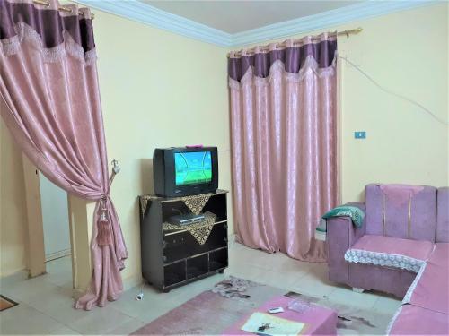 sala de estar con TV y cortinas rosas en Furnished Apartment en Al Minya